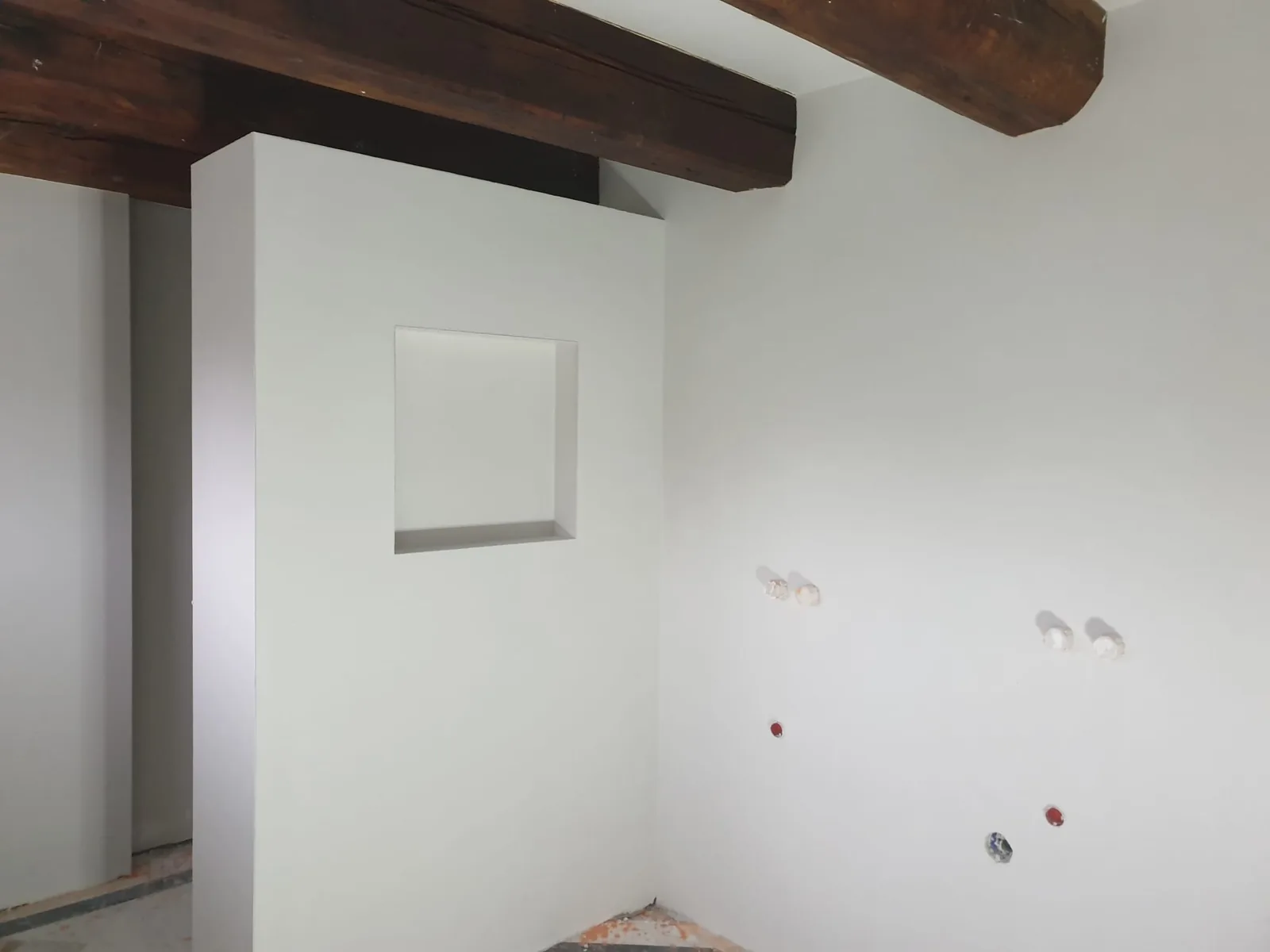 Lichte binnenwand met vierkante nis onder houten plafondbalken
